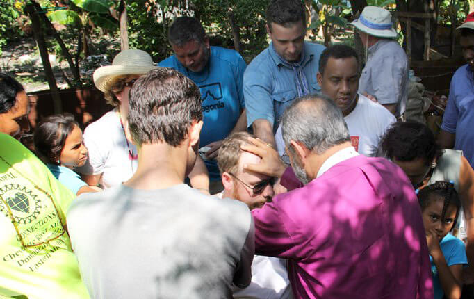Bishop Holguín (purple shirt, back to camera) blesses the Rev. Lonnie Lacy while other team members and local residents gather around.